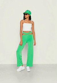 Calças largas verdes com um detalhe de nó na cintura, combinadas com uma t-shirt curta branca e um chapéu de balde verde com padrão. Ténis brancos completam o look.