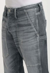 Pantaloni cargo in denim grigio con una miscela di tessuti, dotati di molteplici tasche, una cerniera e rifiniture in metallo argentato.