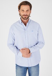 Camicia button-down a righe blu e bianche con maniche lunghe, colletto e orlo arrotondato, realizzata in un tessuto leggero misto cotone.
