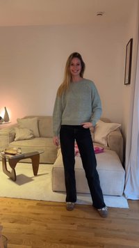 Pull vert clair en maille avec un col rond et des manches bouffantes, associé à un jean noir évasé et des chaussures marron, dans un salon.