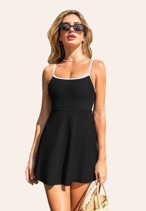 Vestido negro acanalado con ribete blanco, en forma A, con tirantes finos y una falda acampanada. Combinado con gafas de sol de gran tamaño y un bolso de mimbre.