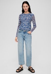 Langarm, blauw patroontop met een golfdesign, gecombineerd met lichtblauwe, losse jeans en zwarte, verstelbare sandalen.