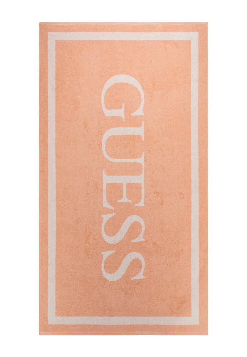 Tappeto color pesca con bordo bianco e grande scritta "GUESS". Texture morbida e design a trama piatta. Adatto per uso interno.