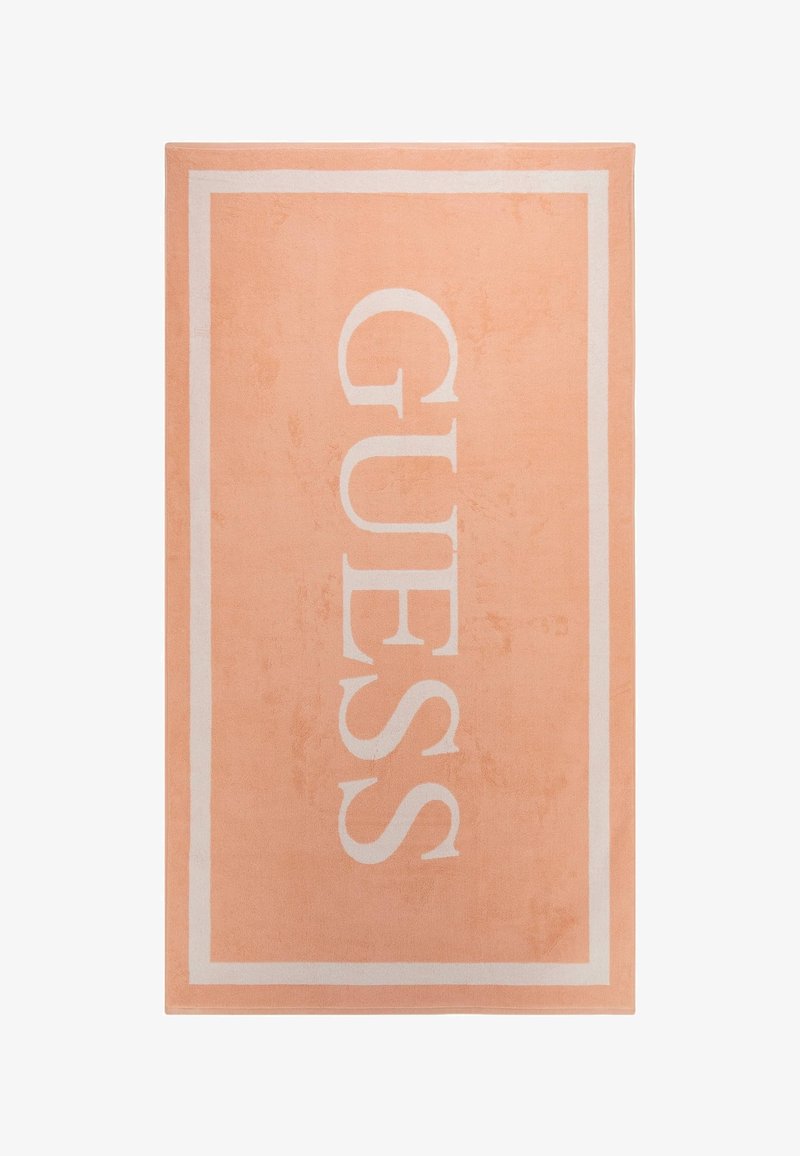 Ferskenfarvet tæppe med hvid kant og stor "GUESS" tekst. Blød tekstur og flad vævningsdesign. Velegnet til indendørs brug.