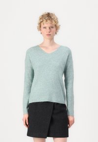 Suéter de malha em teal claro com decote em V, mangas compridas e textura canelada. Combinado com uma saia envolvente cinza escuro. Design suave e casual.