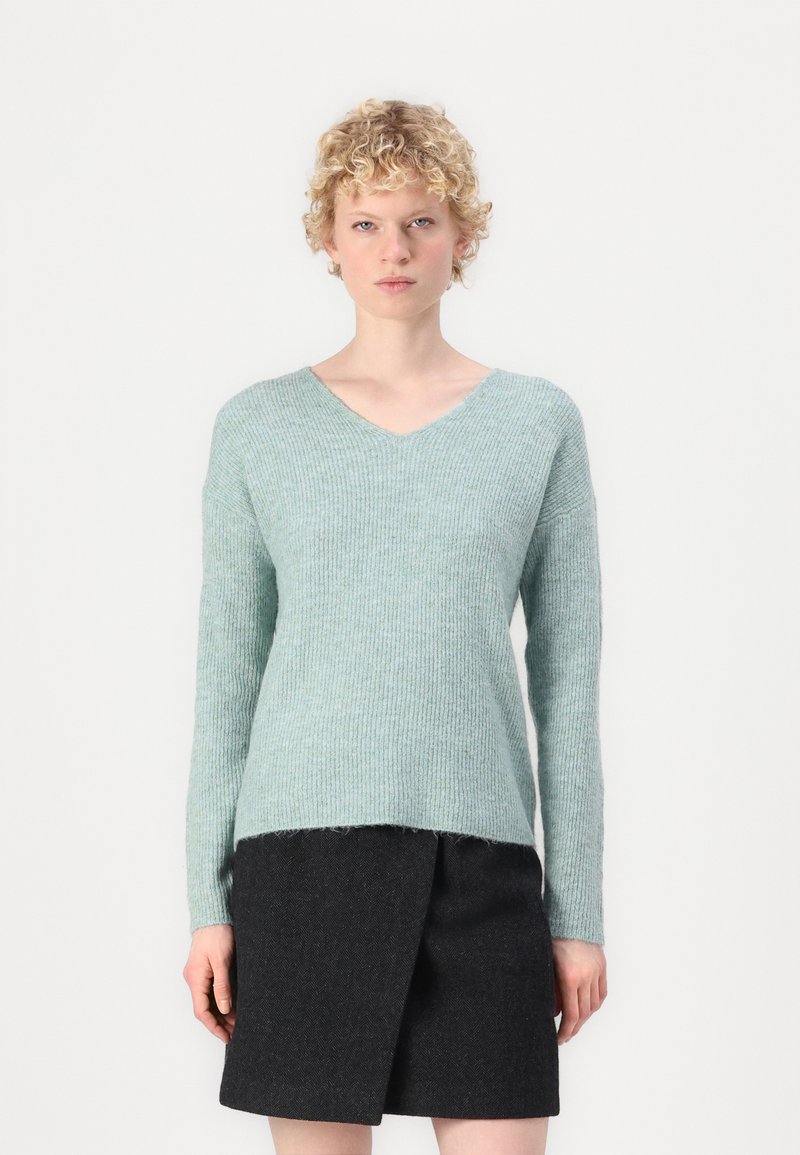 Suéter de malha em teal claro com decote em V, mangas compridas e textura canelada. Combinado com uma saia envolvente cinza escuro. Design suave e casual.
