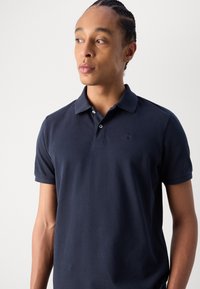 Polo bleu marine en coton, doté d'un col classique, de manches courtes et d'un logo discret sur la poitrine. Texture lisse.