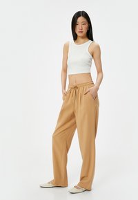 Geknipte witte ribben tanktop, tan trekkoordbroek met zakken, gladde stof, relaxte pasvorm, gecombineerd met lichtgekleurde platte schoenen.