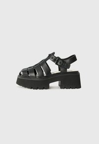 Sandali platform neri realizzati in materiale morbido, caratterizzati da fasce larghe, una chiusura con fibbia e una suola in gomma texturizzata con design massiccio.