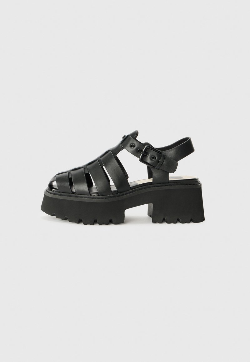 Sandali platform neri realizzati in materiale morbido, caratterizzati da fasce larghe, una chiusura con fibbia e una suola in gomma texturizzata con design massiccio.