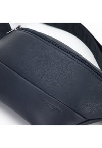Marsupio in pelle blu navy con finitura testurizzata, dotato di chiusura con zip e pannello frontale piatto impresso con il nome del marchio.