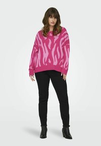 Pulover supradimensionat de culoare roz aprins, cu dungi zebra de un roz mai deschis, având manșete și tiv cu dungi, asortat cu blugi negri ajustați și botine.