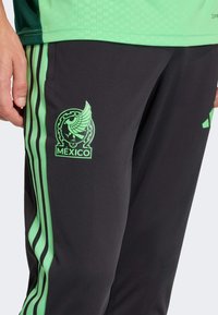 Črne športne hlače z zelenimi črtami, z izrazitim zelenim emblemom México na stegnih in zelenim logotipom Adidas.