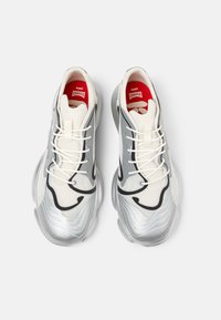 Sneakers bianchi e argentati con design ondulato, caratterizzati da accenti neri, tomaia in mesh testurizzato e lacci bianchi. Soletta rossa con marchio.