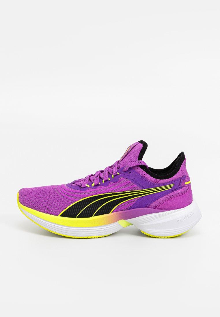 Zapatilla de correr morada con una parte superior de punto, acentos negros, entresuela amarilla y suela blanca. Presenta un diseño elegante y una superficie texturizada.