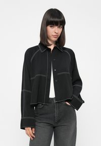 Svart cropped skjorte med hvite sømdetaljer, knappelukking og lange ermer, kombinert med høyhåret grå denim.