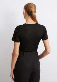 Top nero a maniche corte con texture a coste e scollatura rotonda, abbinato a pantaloni neri a vita alta. Il design è aderente e minimalista.