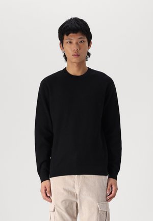 Pull noir à côtes avec un col rond, des manches longues et une coupe décontractée, associé à un pantalon en velours côtelé beige clair avec poches latérales.