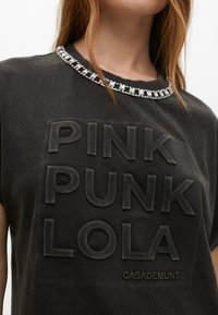 Black cotton t-shirt featuring raised text "PINK PUNK LOLA CASADEMUNT" and a decorative rhinestone collar.