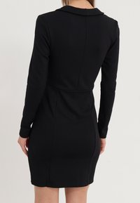 Schwarzes, langärmliges Kleid mit figurbetontem Schnitt, klassischem Kragen, glattem Stoff und dezenten Nahtdetails entlang des Rückens.