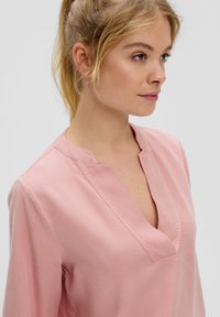 Roze blouse met een V-hals en lange mouwen, gemaakt van zachte stof. Kenmerkt zich door een eenvoudig ontwerp en een kraagloze halslijn.