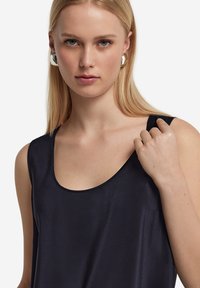 Marinblå ärmlös topp med rund halsringning, tillverkad av ett mjukt material. Modellen bär en enkel design som framhäver tygets subtila lyster.