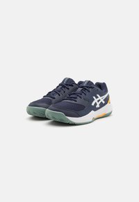 Zapatillas deportivas en color azul marino con una parte superior de malla transpirable, acentos en blanco y naranja, y una suela de goma verde texturizada para tracción.