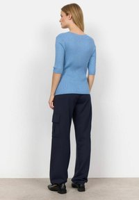 Blaues, geripptes Langarmoberteil mit taillierter Passform, kombiniert mit lockeren, marineblauen Cargo-Hosen mit seitlichen Taschen. Mattschwarze Schuhe runden den Look ab.