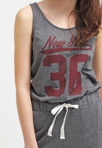 Canottiera grigia con grafica rossa "New 36". Morbido misto cotone, scollatura rotonda e vestibilità morbida. Abbinata a pantaloni grigi con cordino bianco.