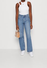 Top blanco sin mangas con el logo de Nike, jeans de tiro alto en un tono azul claro, zapatillas blancas y un pequeño bolso marrón claro con detalles en plateado.