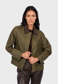 Oliwkowa skórzana kurtka z brązowym kordowym kołnierzem, z przodu na zatrzaski oraz z bocznymi kieszeniami. Gładka tekstura, lekko luźny krój.