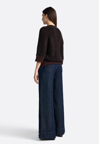 Maglione morbido marrone scuro con orlo a coste, abbinato a jeans in denim scuro a gamba larga con tasche posteriori, visto da dietro.