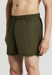 Olivgrüne Badehosen aus strukturierter Stoffqualität, mit elastischem Bund und Kordelzug, Seitentaschen und einer lockeren Passform.