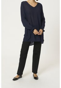 Marineblå langærmet tunika med V-hals, der har en afslappet pasform og knapdetaljer, kombineret med sorte bukser med lige ben og sorte flade sko.