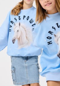 Fénykék pulóver nagy, fehér ló grafikával, fekete "HORSEPOWER" felirattal, és farmer szoknya oldalsó zsebekkel.