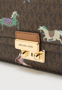 Bolso de tela marrón con textura que presenta gráficos coloridos de caballos. Cierre con herrajes en tono dorado y placa con el nombre "MICHAEL KORS" en relieve.
