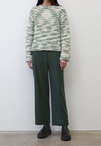 Maglione lavorato a maglia in un motivo camouflage crema e verde, con maniche lunghe e scollo rotondo, abbinato a pantaloni a gamba larga verde scuro e stivali neri con suola spessa.
