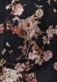 Prim-plan al unui buzunar din material textil negru, cu un model floral detaliat în nuanțe de roz, maro și bej.