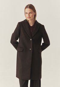 Bruine wollen blazerjas met geklapte revers, twee knopen en voorzakken. Strakke lijnen en een getailleerd silhouet.