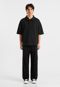 Sort polo t-shirt med krave i oversized pasform. Kombineret med sorte sweatpants med sidelindninger. Simpelt design og blød tekstur.