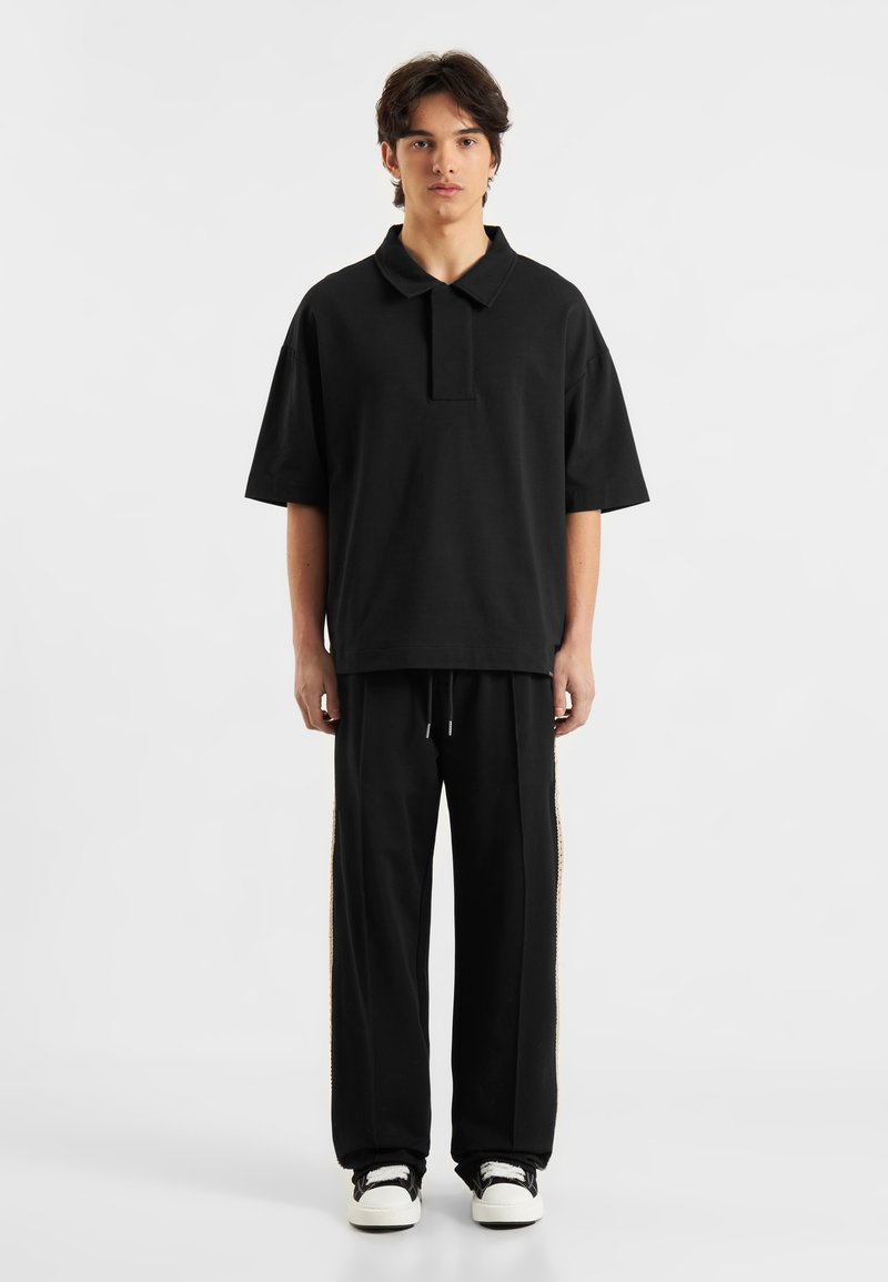 Sort polo t-shirt med krave i oversized pasform. Kombineret med sorte sweatpants med sidelindninger. Simpelt design og blød tekstur.