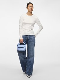 Top aderente bianco a maniche lunghe, jeans larghi a vita alta blu, tiene in mano una piccola borsa a tracolla azzurra, scarpe bianche e nere, sfondo neutro.