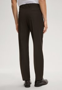 Dunkelbraune, maßgeschneiderte Hosen mit geradem Schnitt und zwei Gesäßtaschen. Glatte Stofftextur, kombiniert mit schwarzen Anzugschuhen.