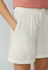 Shorts blancs texturés avec une taille élastique, détail de cordon de serrage et poches latérales, présentant un design en tissu légèrement froissé.