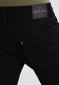 Vaqueros de denim negro con una textura suave, presentan una etiqueta de cuero marcada "LEVI'S LINE 8" y dos bolsillos traseros con costuras sutiles.