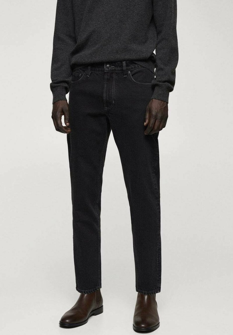 Jeans de mezclilla negra con un corte recto, diseño de cinco bolsillos y costuras en contraste, combinados con un suéter oscuro y botas tobilleras marrones.