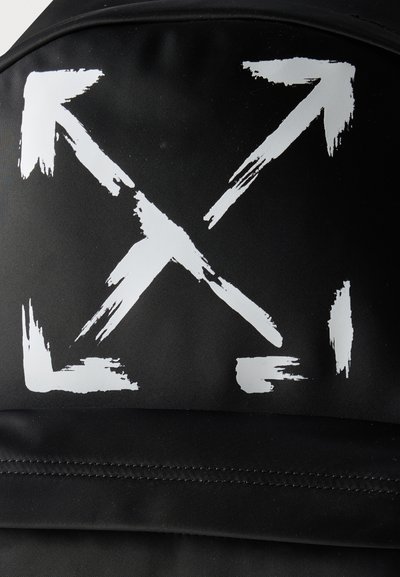 Τέσσερα λευκά βέλη σε στυλ πινελιάς που δείχνουν διαγώνια προς τα έξω σε μαύρο ύφασμα, σχηματίζοντας ένα σχήμα X.