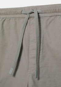 Pantalon en tissu gris avec une ceinture élastique et un cordon gris noué pendant au centre devant.