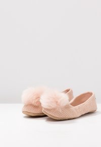 Růžové pletené pantofle s texturovaným svrškem, kulatými huňatými pom-pomy na přední části a měkkou, flexibilní podrážkou.