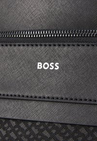 Black textured fabric with a subtle pattern, featuring a horizontal zipper and the white text "BOSS" centered on the surface.